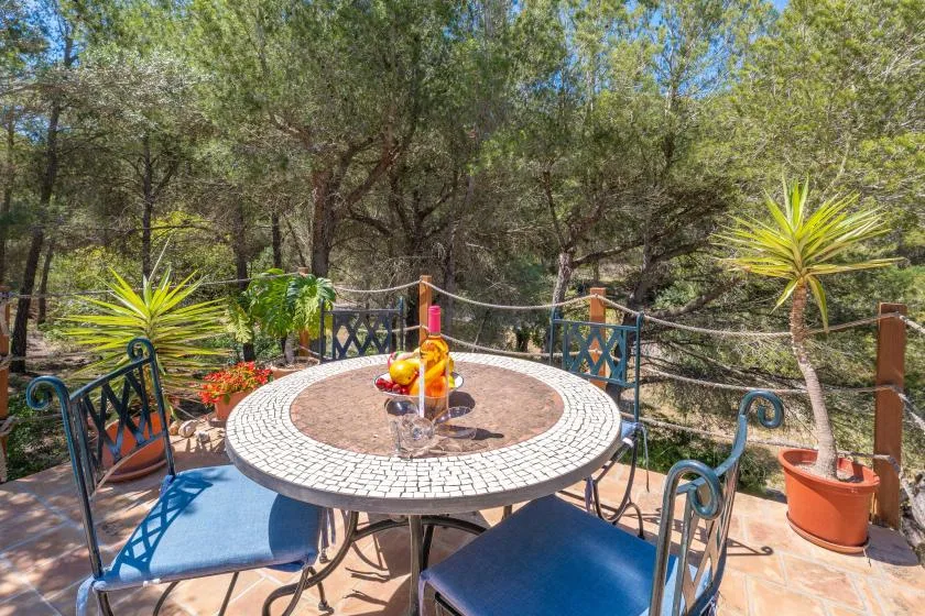 An outdoor patio has a round mosaic table surrounded by blue seating and trees.