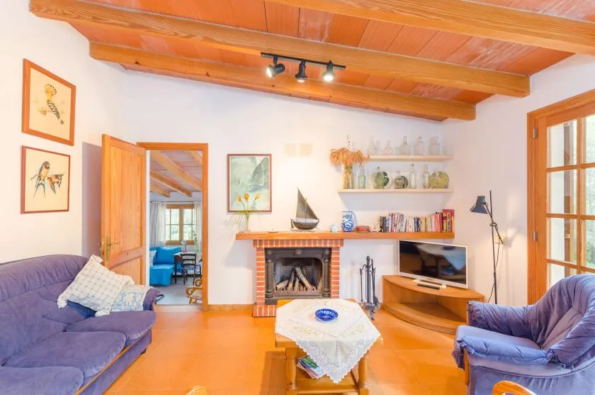 A warm living room with purple seating, a fireplace, and exposed wooden ceiling beams.