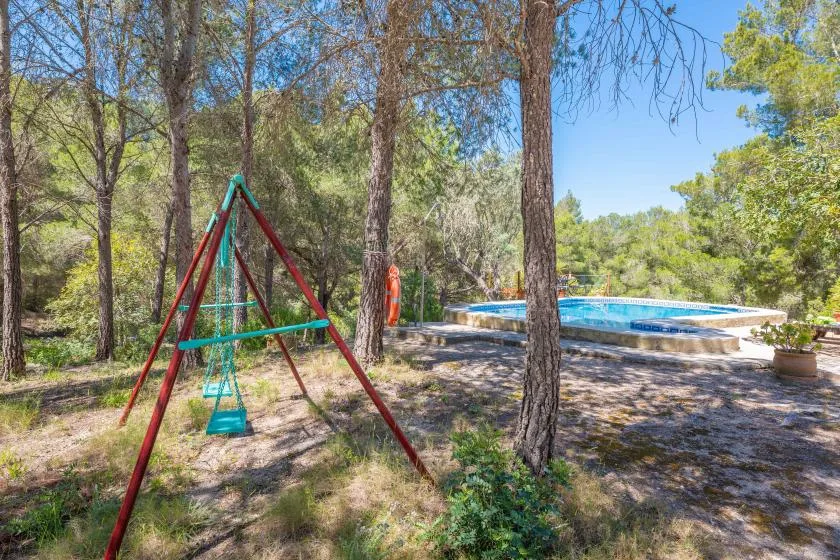A wooded outdoor area with a swing set beside a swimming pool.