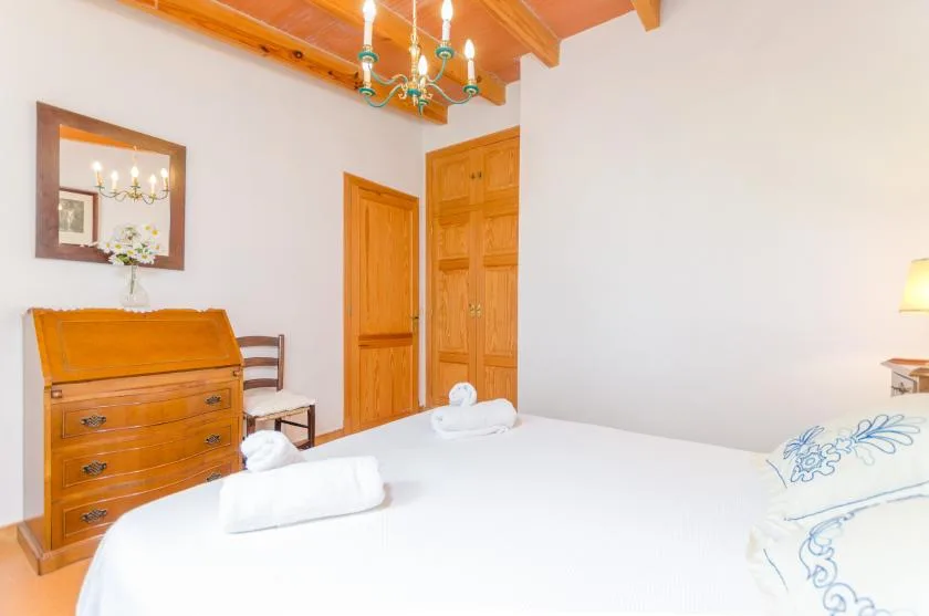 A bedroom with a neatly made bed, wooden furnishings, and a ceiling chandelier.