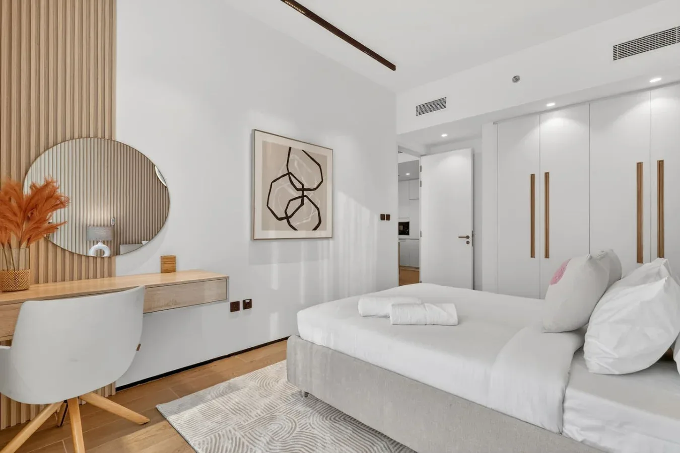 Un dormitorio luminoso con una cama blanca, un escritorio y armarios empotrados.