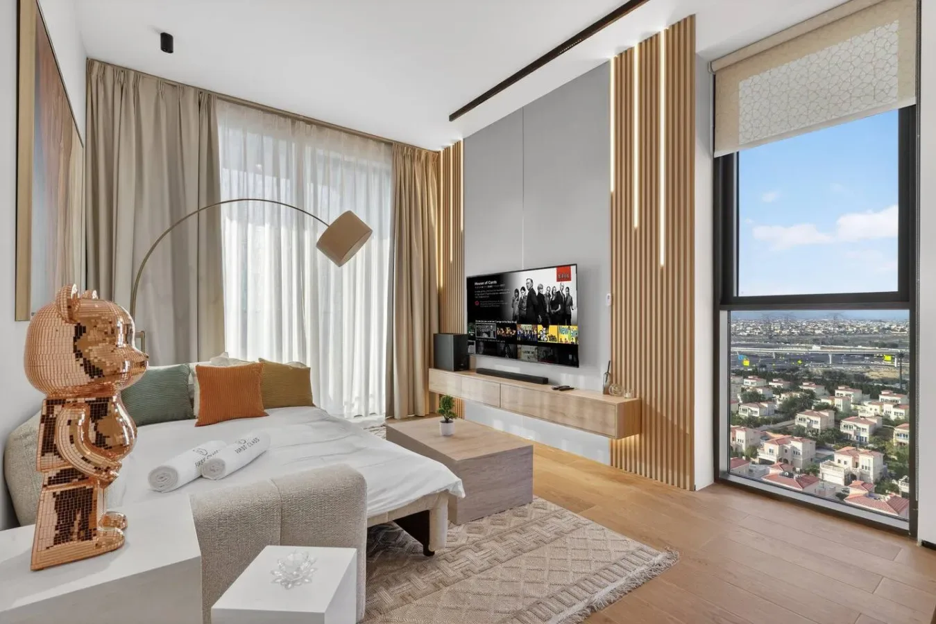 Un dormitorio luminoso con cama, televisor y grandes ventanas con vistas a la ciudad.