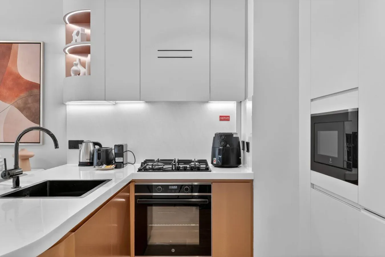 Una cocina moderna con encimeras blancas, gabinetes de tonos madera y electrodomésticos integrados.