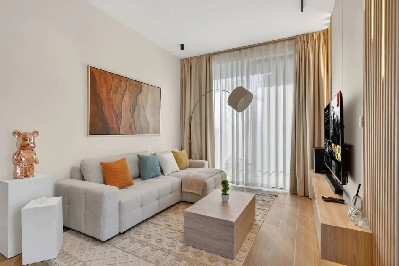 Una sala de estar con sofá seccional, mesa de centro y una gran ventana con cortinas.