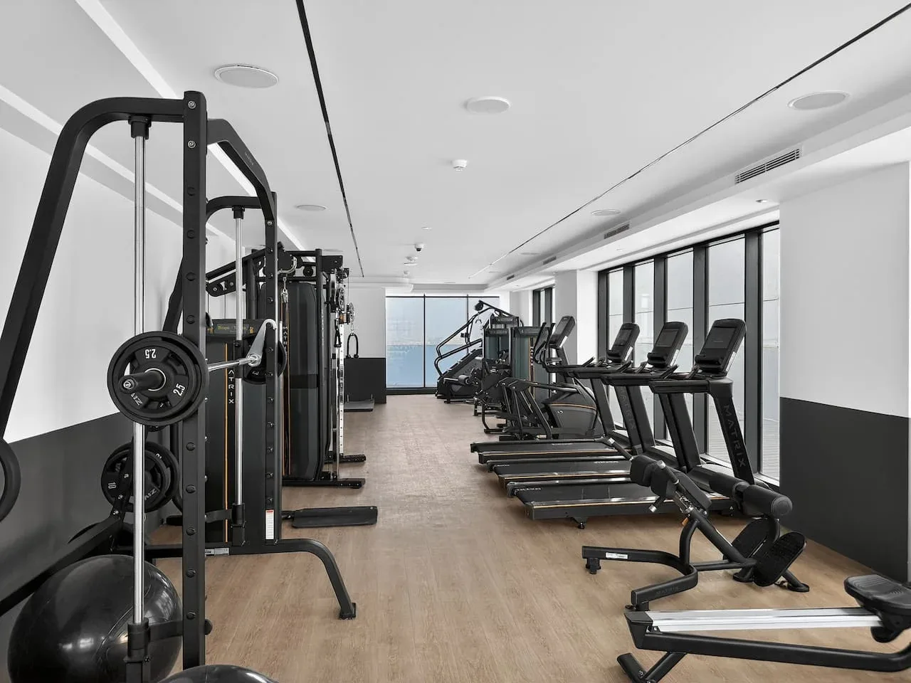 Un gimnasio con máquinas de ejercicio y cintas de correr junto a las ventanas.