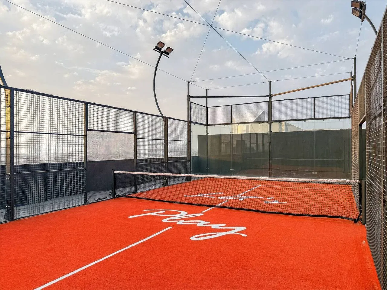 Una pista de pádel al aire libre con superficie roja y una cerca de malla alrededor.