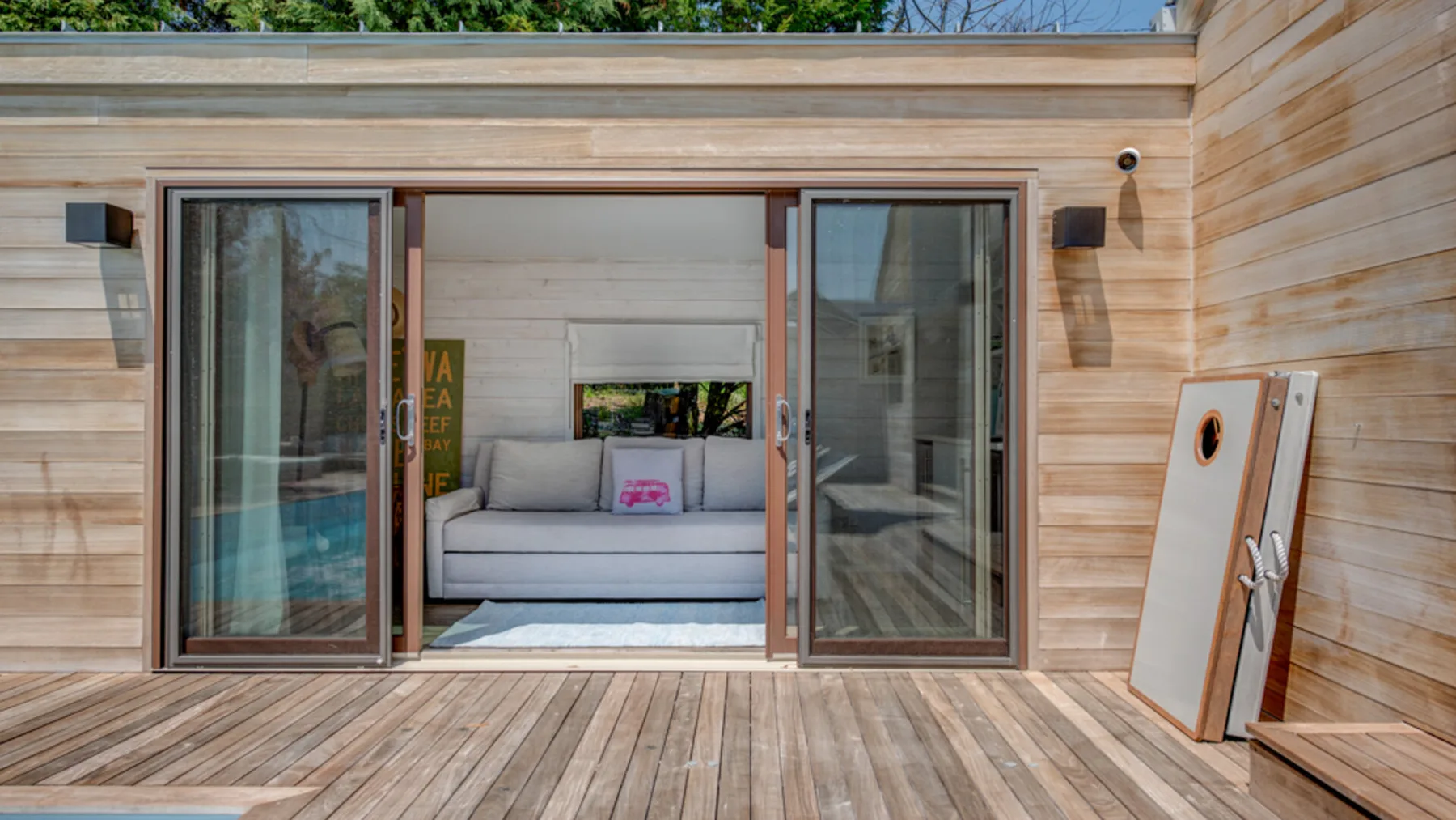 A wooden deck opens onto a lounge with a sofa and sliding glass doors.