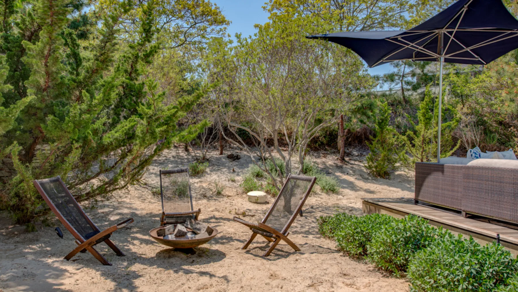 An outdoor seating area with a small fire pit among trees and shrubs.