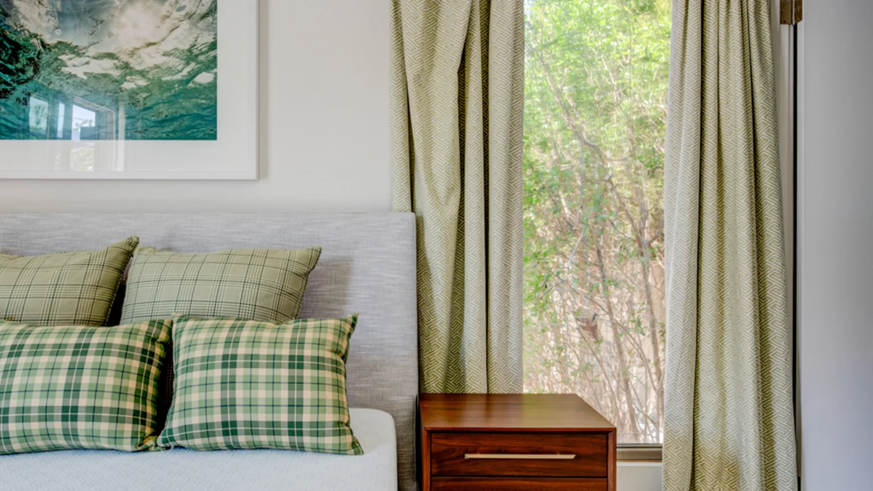 A bedroom with a bed, plaid pillows, and a window framed by curtains.