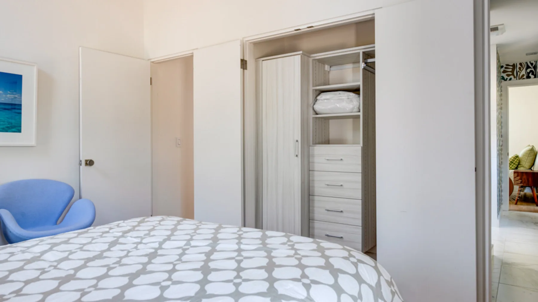 A bedroom with a patterned bedspread, blue seating, and an open wardrobe.