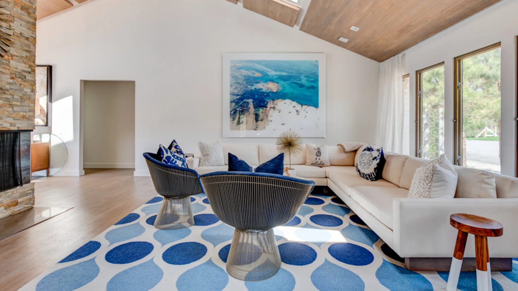 A bright living room with a white sectional and round tables on a blue patterned rug.