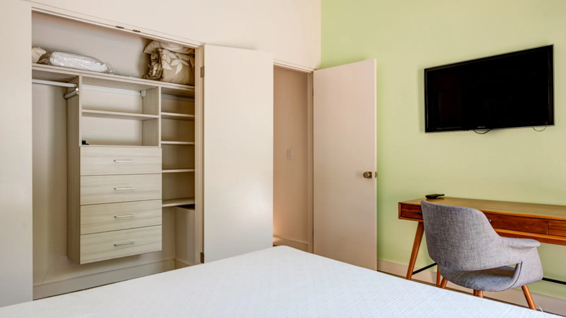 A bedroom with an open wardrobe and a wall-mounted television.