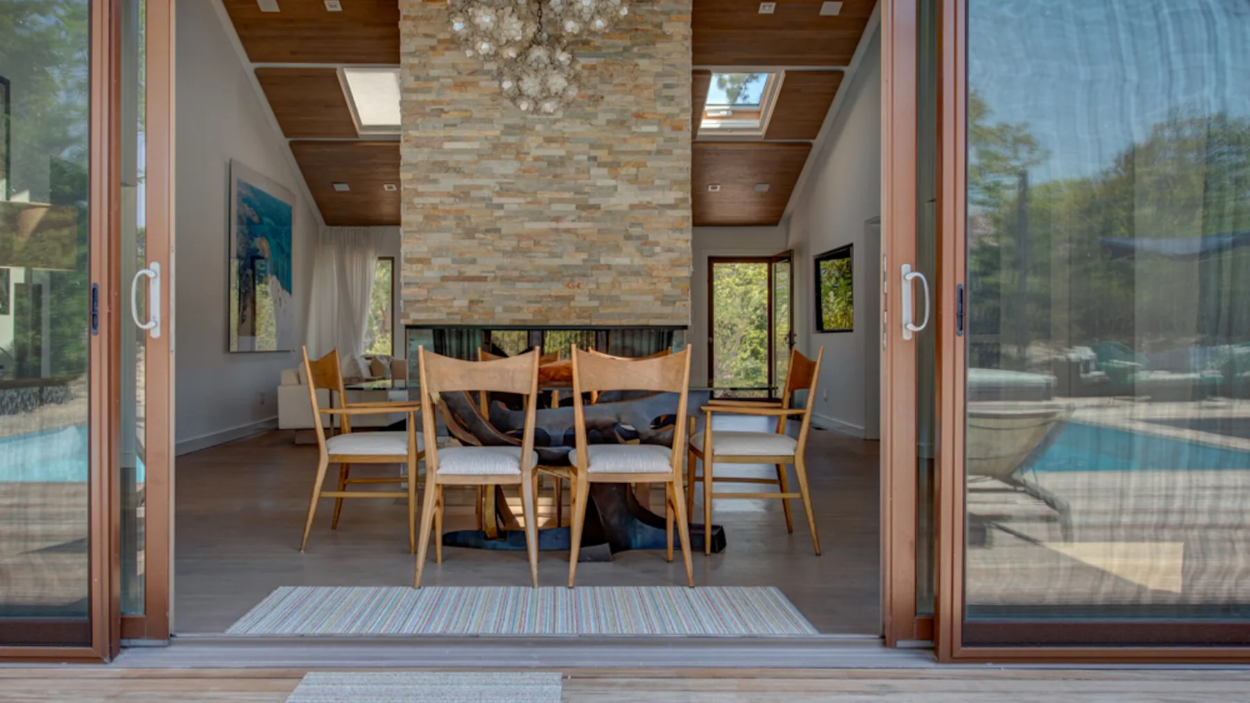 A dining area with a long table and chairs sits beneath a stone fireplace.