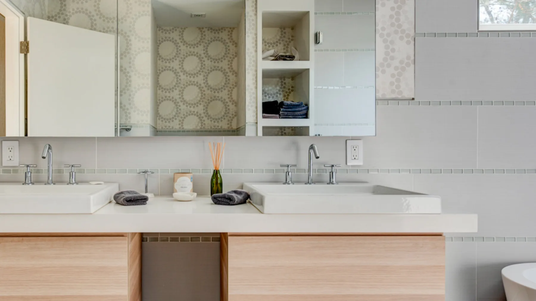 A bathroom vanity with two sinks, light wood cabinetry, and patterned wall panels.