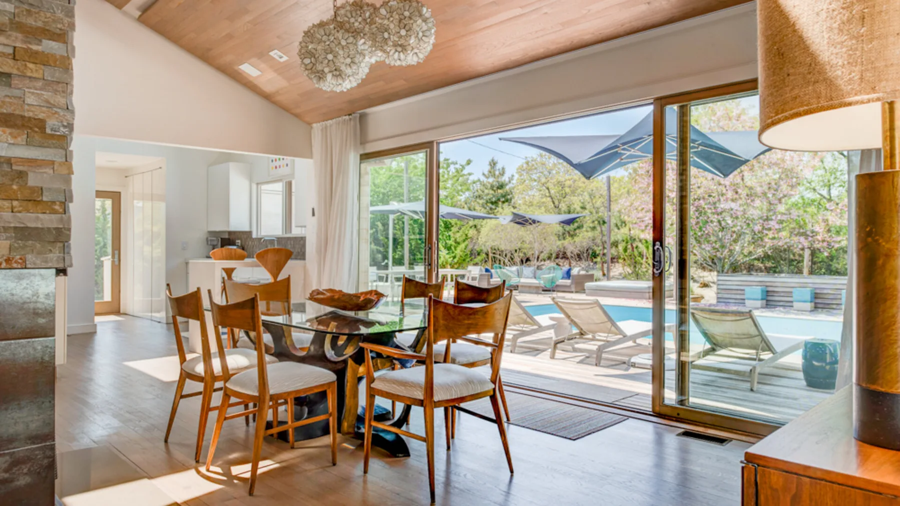 A dining area with a wooden table beside large windows overlooking a pool.