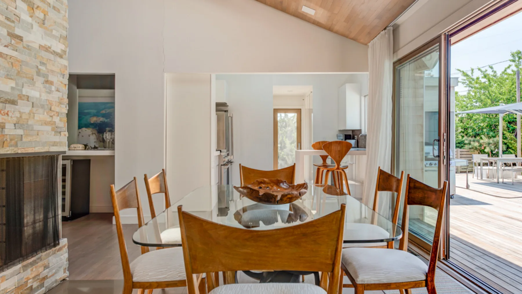 A bright dining area with a glass table and large windows opening onto a deck.