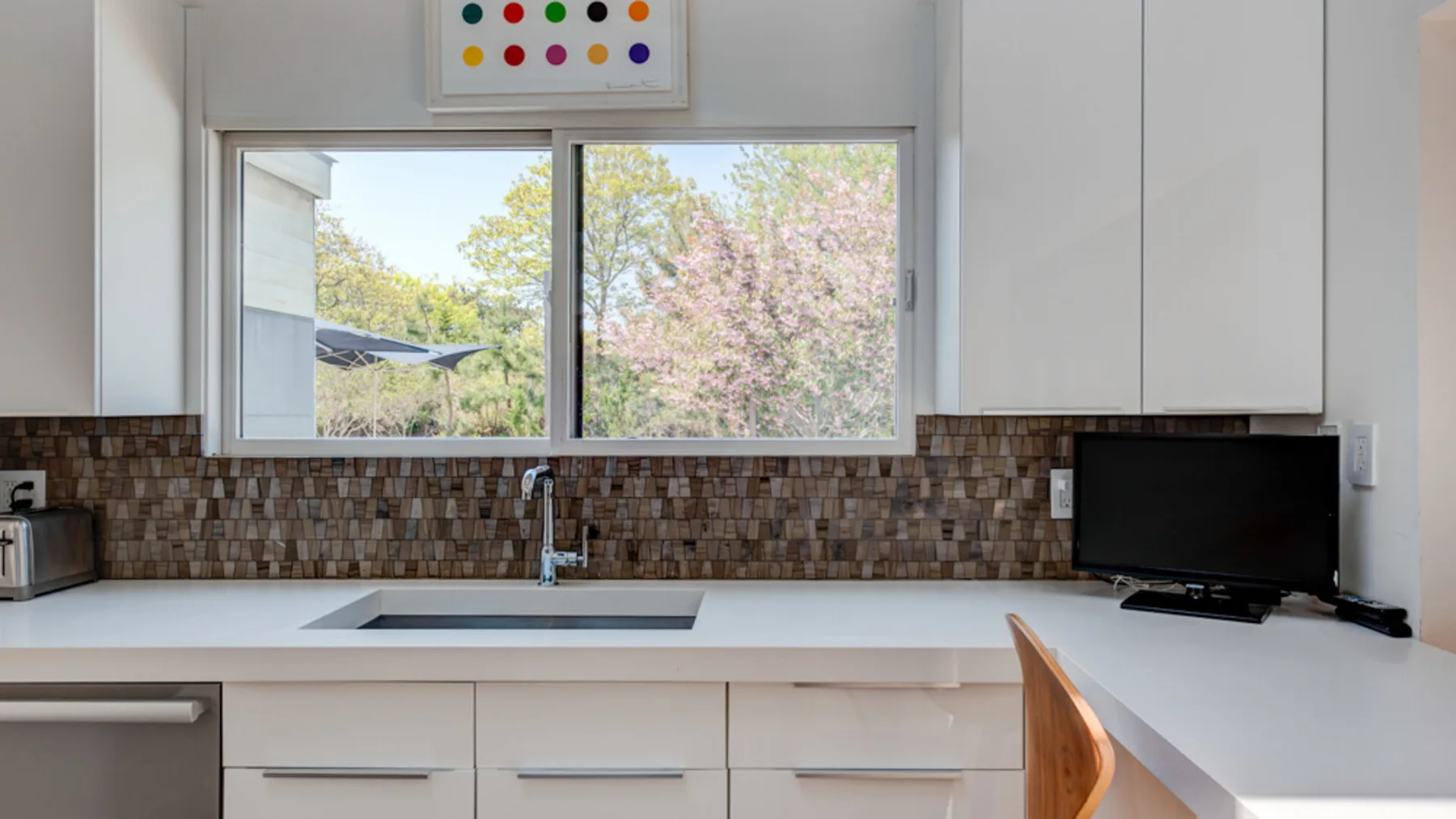 A bright kitchen with a sink beneath a wide window overlooking trees.