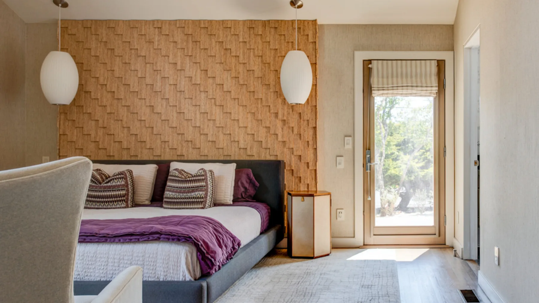 A bedroom with a bed against a textured wall and a glass door opening to a bright view.
