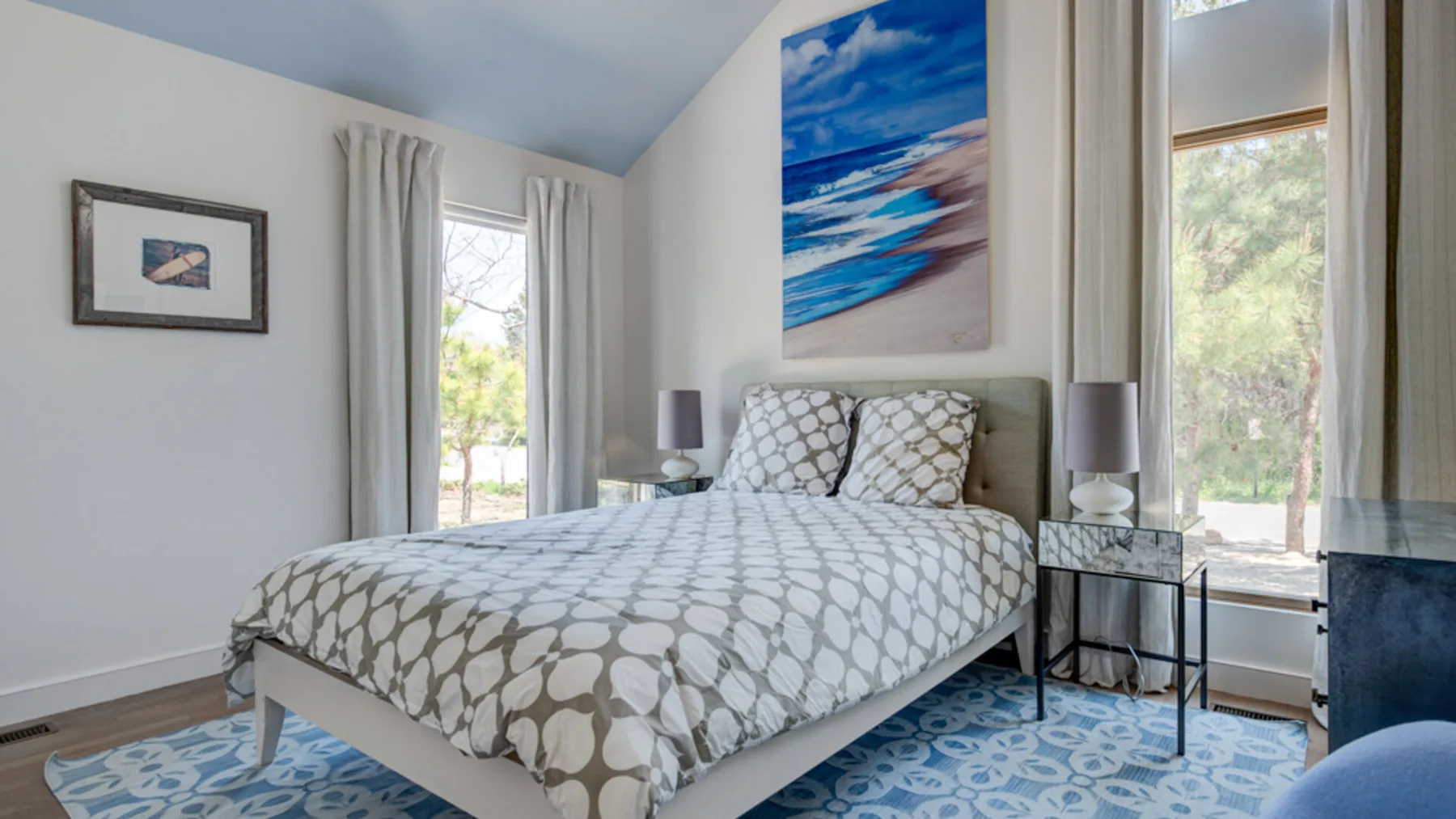 A bedroom with a bed beneath a colorful ocean painting.