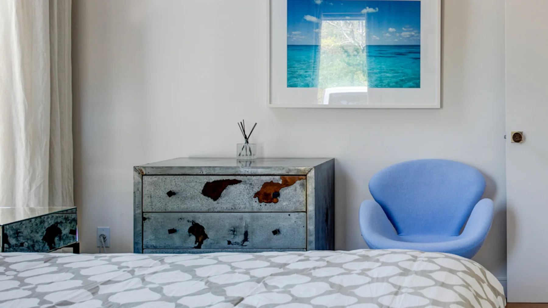 A bedroom with a patterned bedspread, a dresser, and a blue chair.