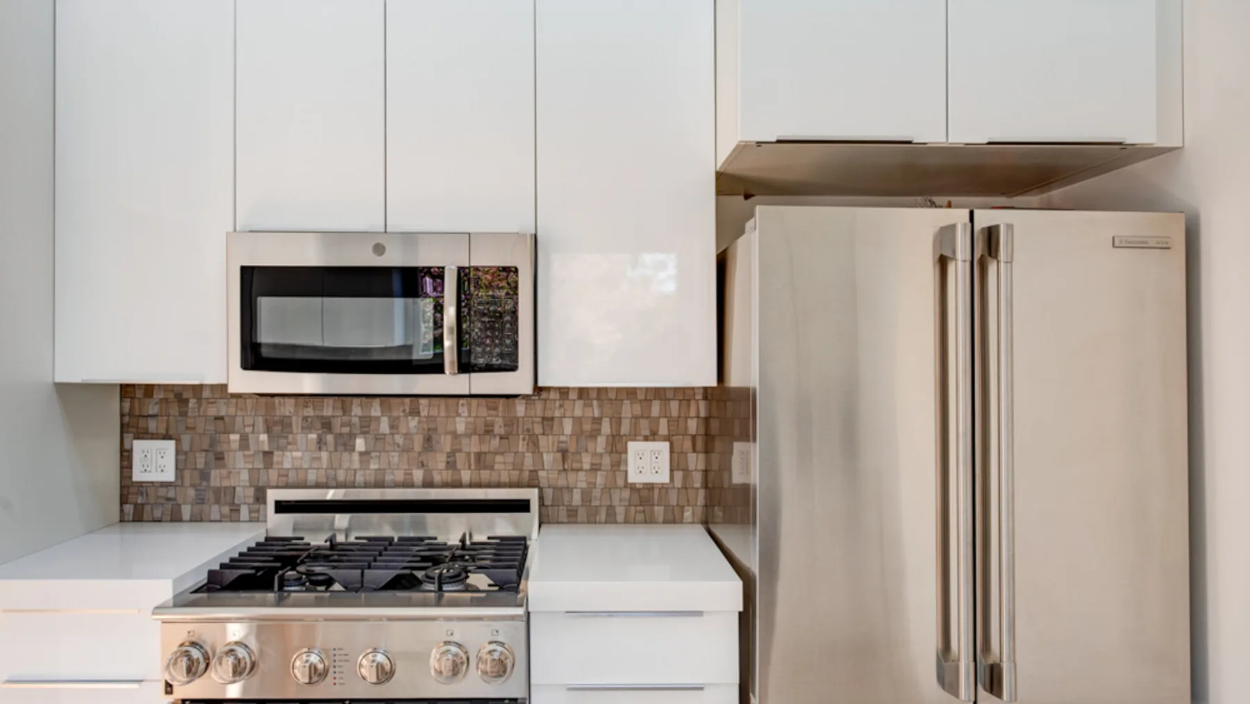 A compact kitchen with white cabinets, a stove, microwave, and refrigerator.