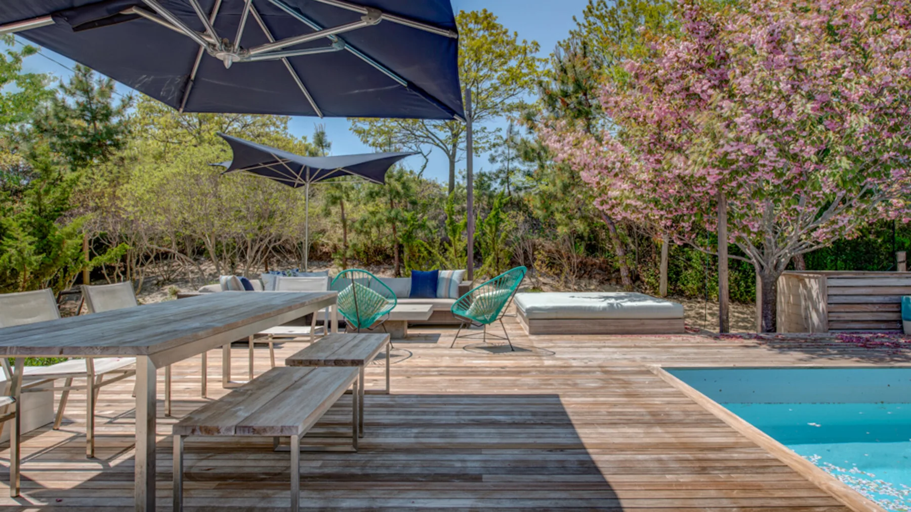 An outdoor wooden deck with a swimming pool, table, and shaded seating.