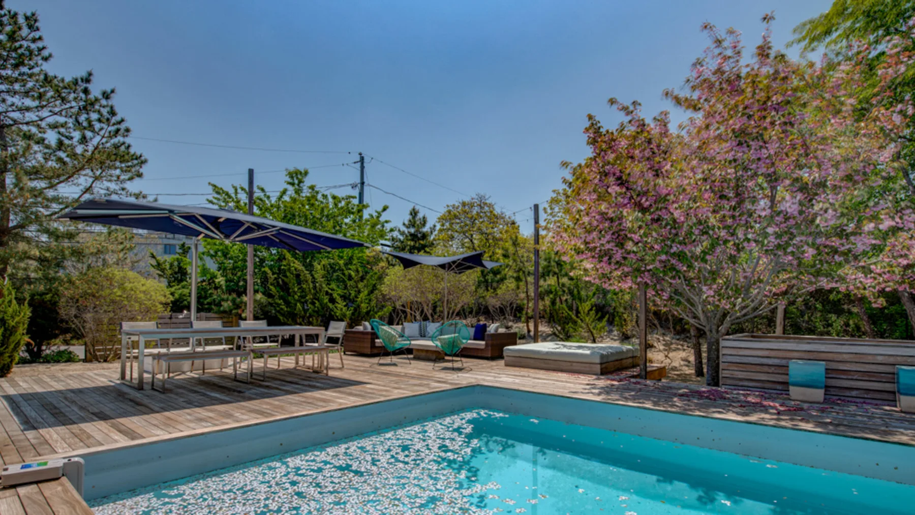 An outdoor swimming pool sits beside a wooden deck with shaded seating.