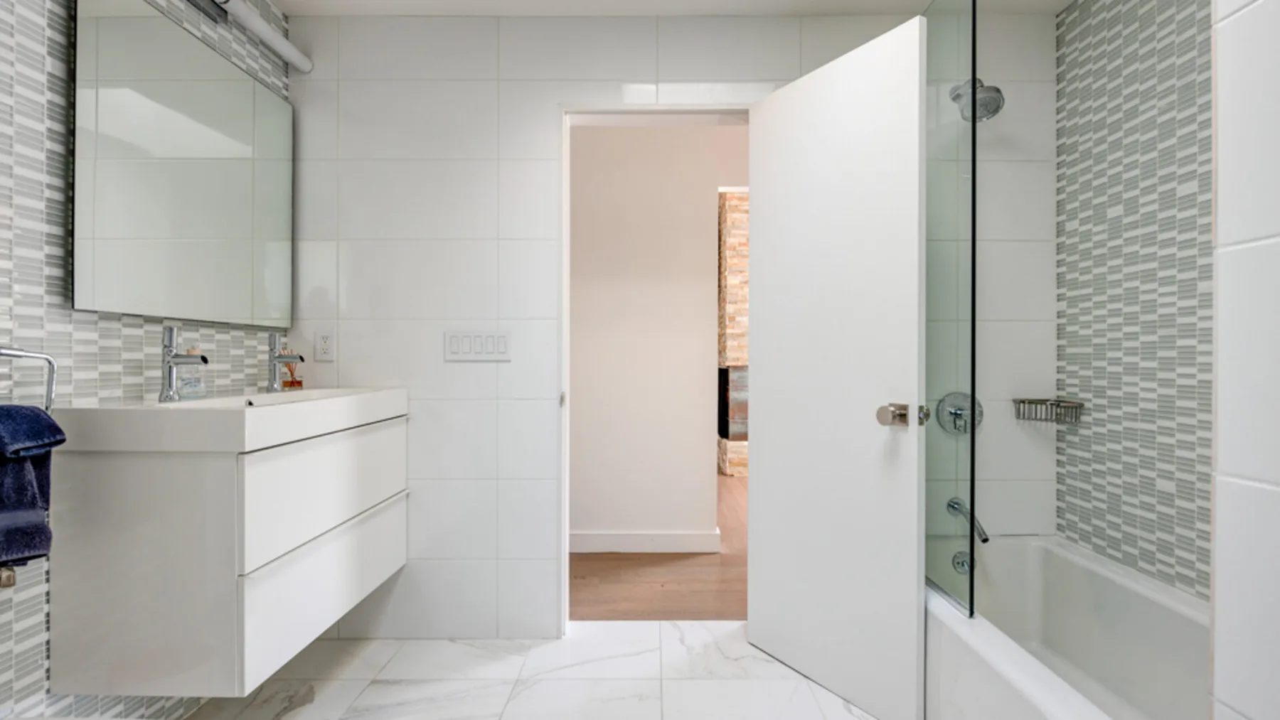 A bright bathroom with a floating vanity, wall mirror, and bathtub.