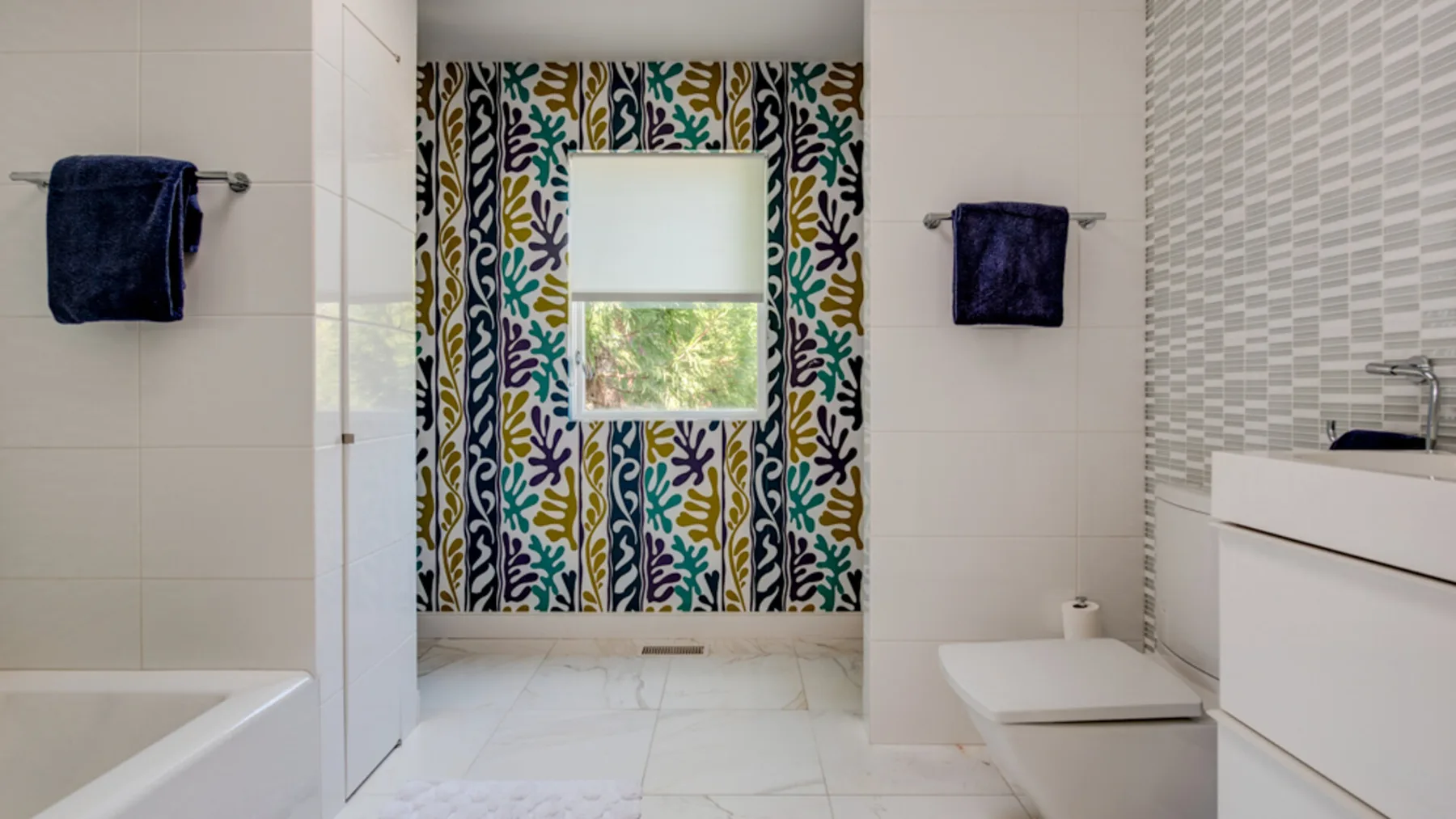 A tiled bathroom with a bathtub, toilet, and patterned window curtains.