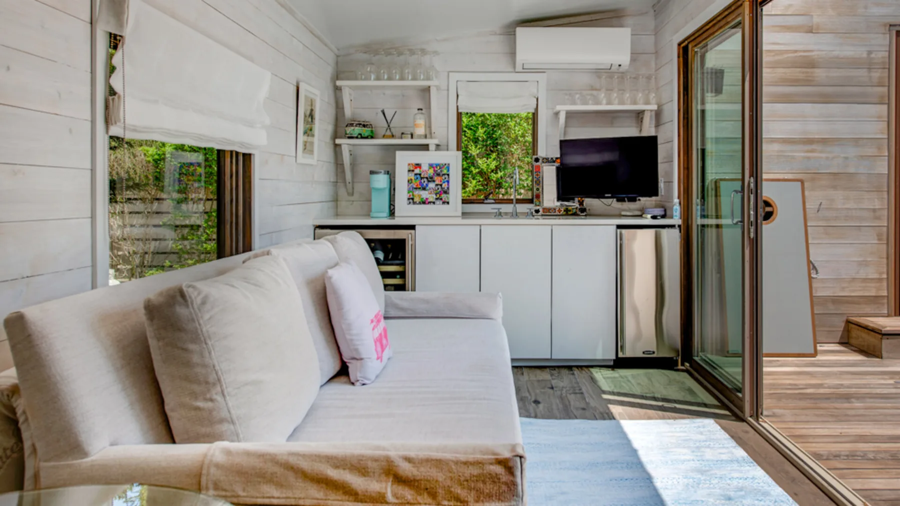 A bright living room with a sofa, television, and large glass doors.
