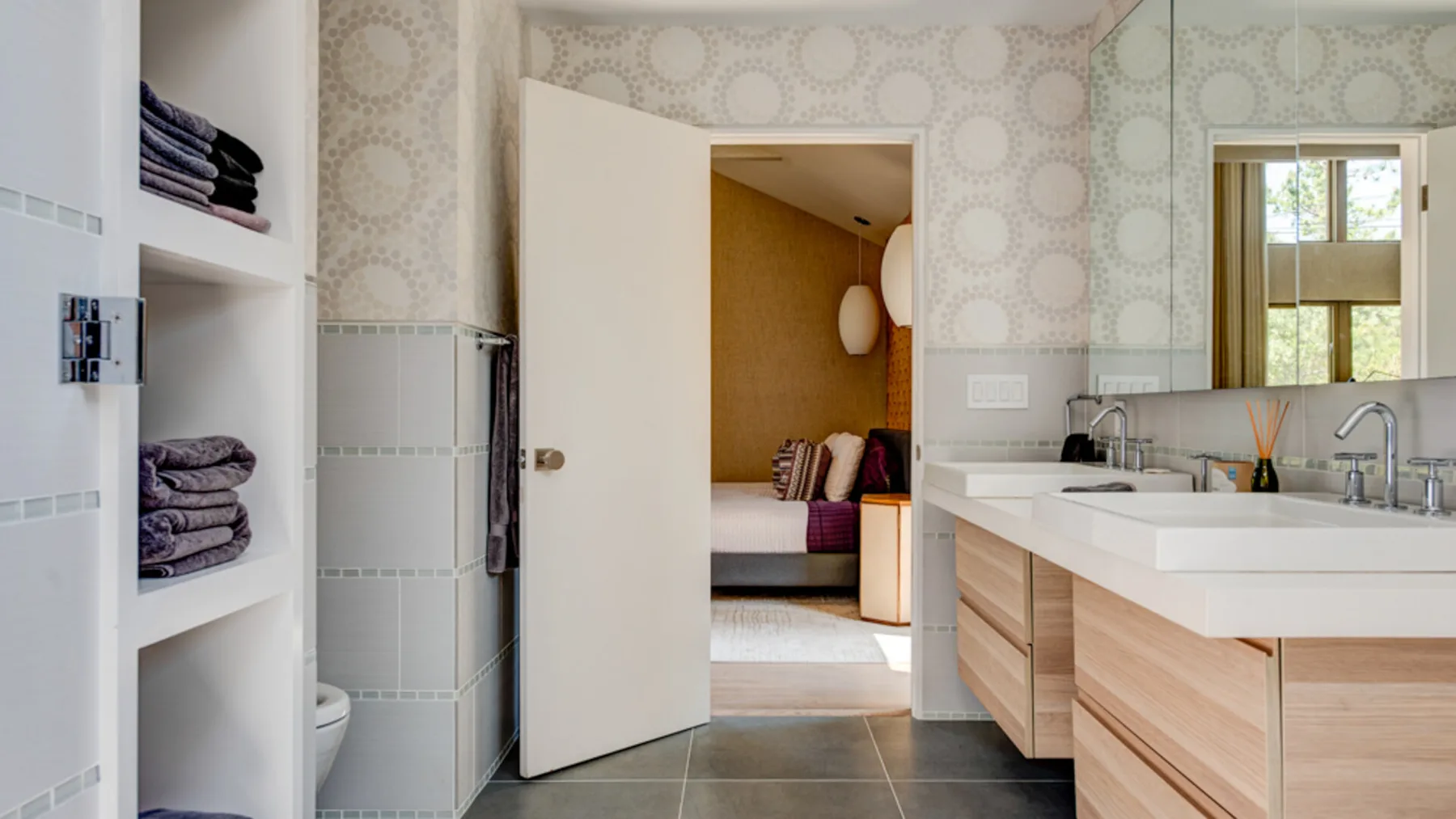 A bathroom with a long vanity and an open doorway to an adjoining room.
