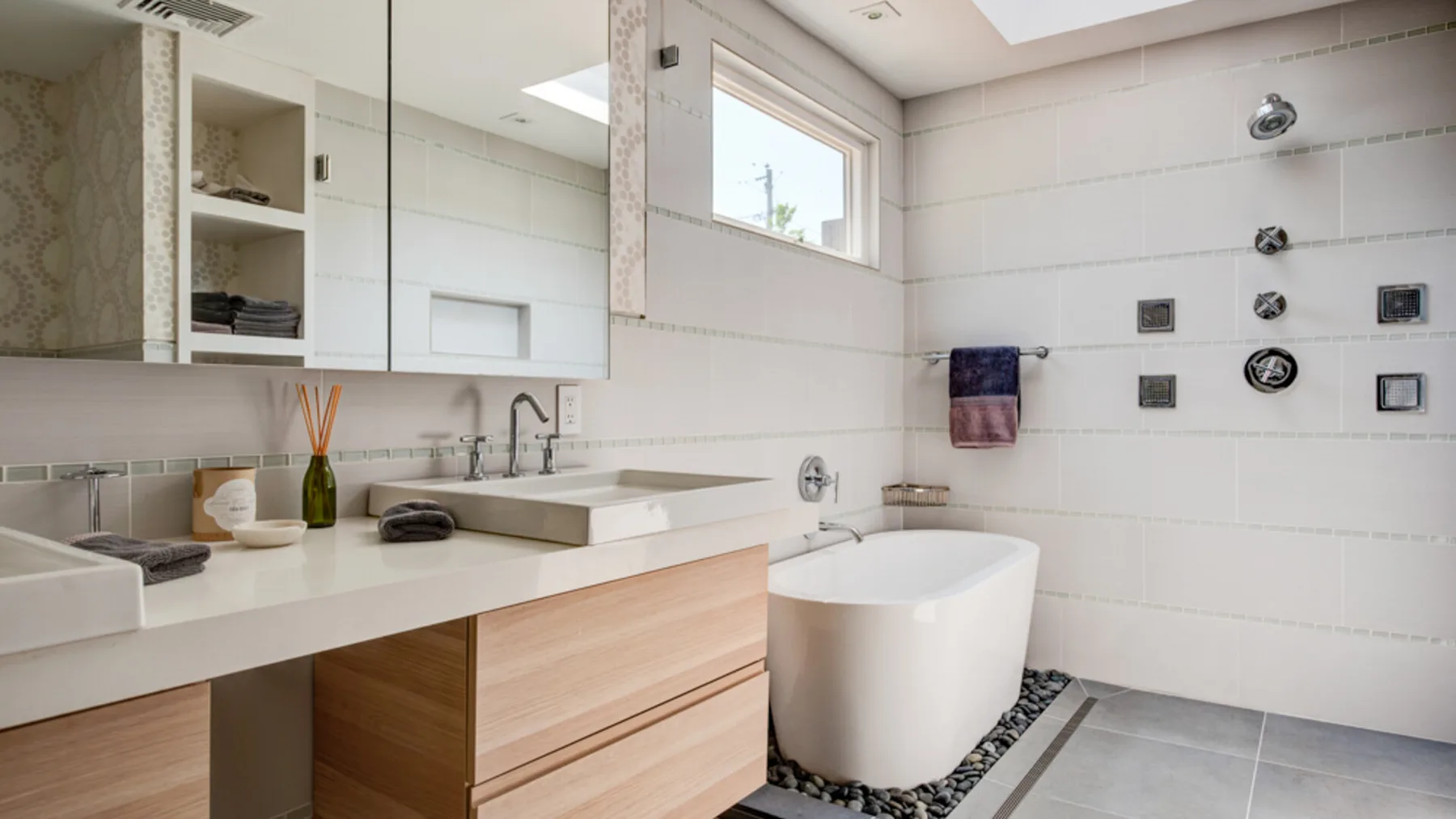 A bright bathroom features a vanity, large mirror, and freestanding bathtub.