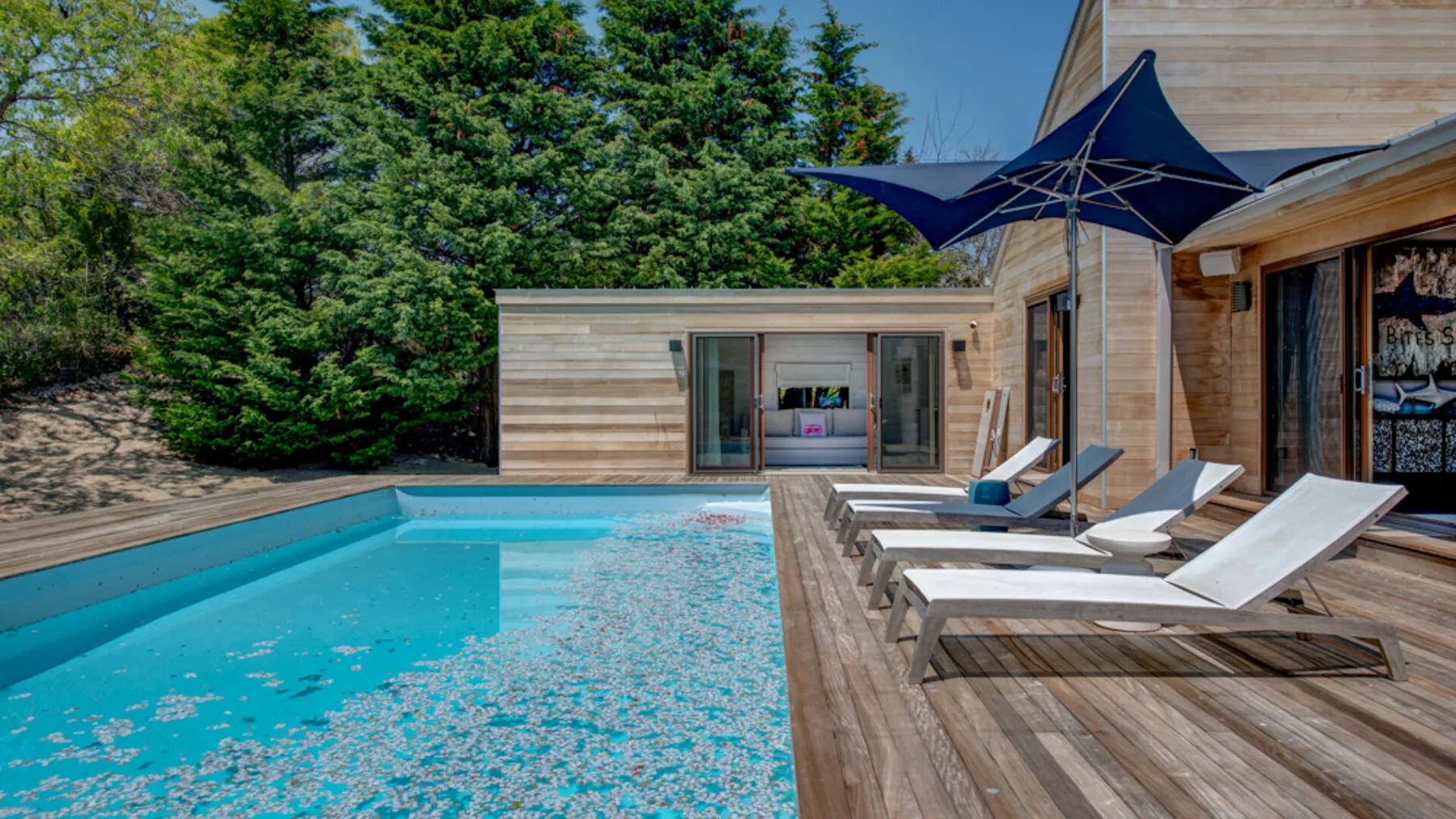 An outdoor swimming pool beside a wooden deck with lounge seating.
