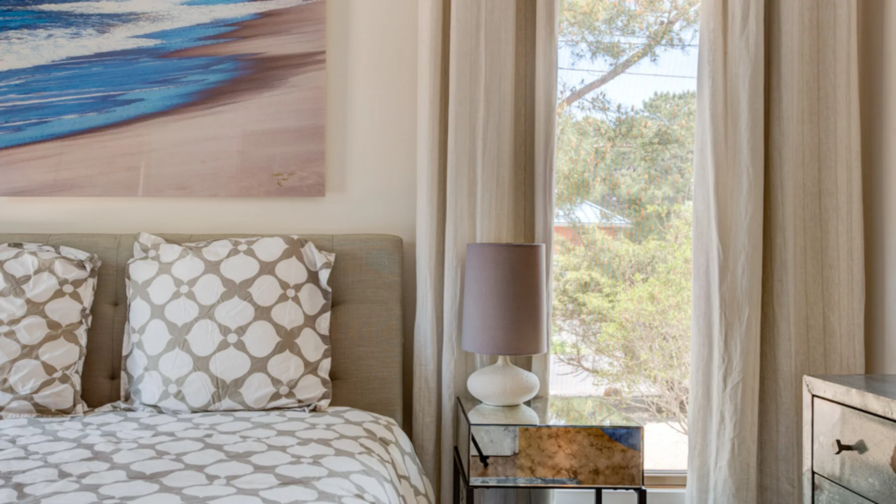 A bedroom with a patterned bed beside a window and curtains.