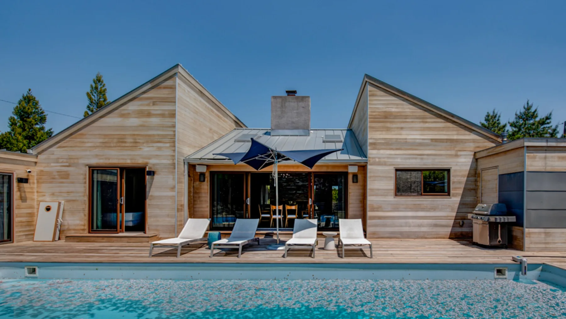 A modern house opens onto a swimming pool, with lounge seating on the patio.
