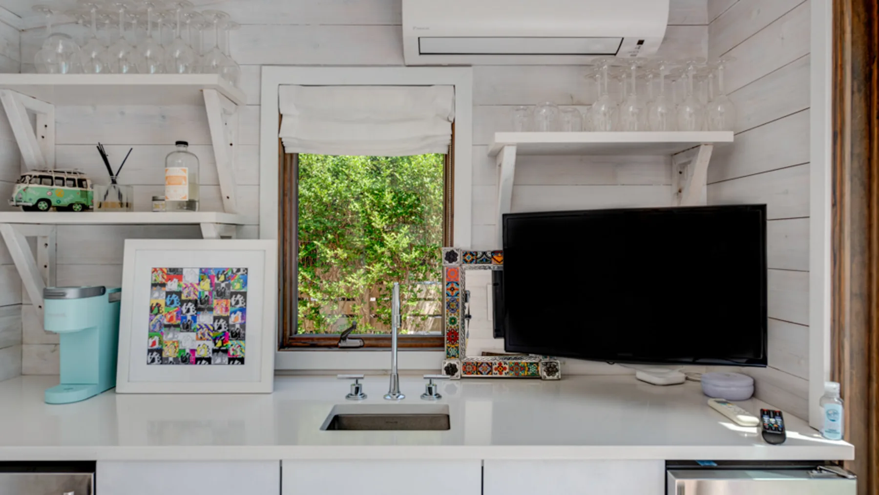 A bright kitchenette with a sink beneath a window and a television on the counter.