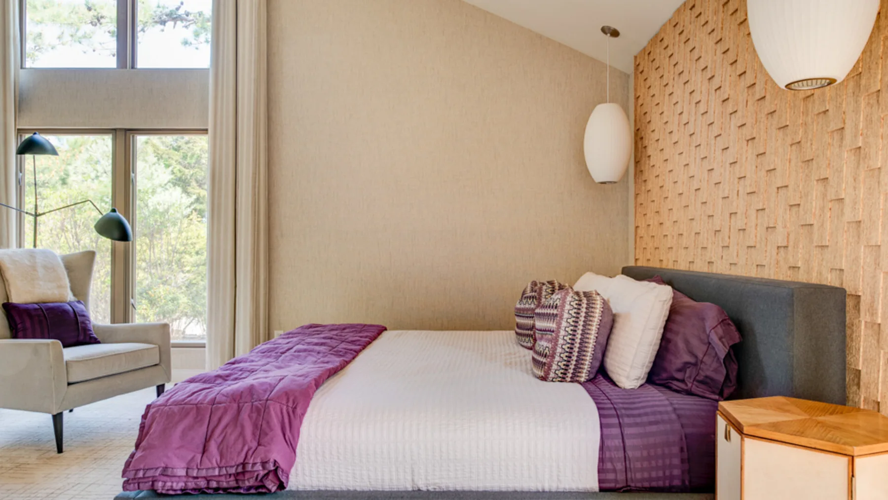 A bedroom with a white bed, purple bedding, and a large window.