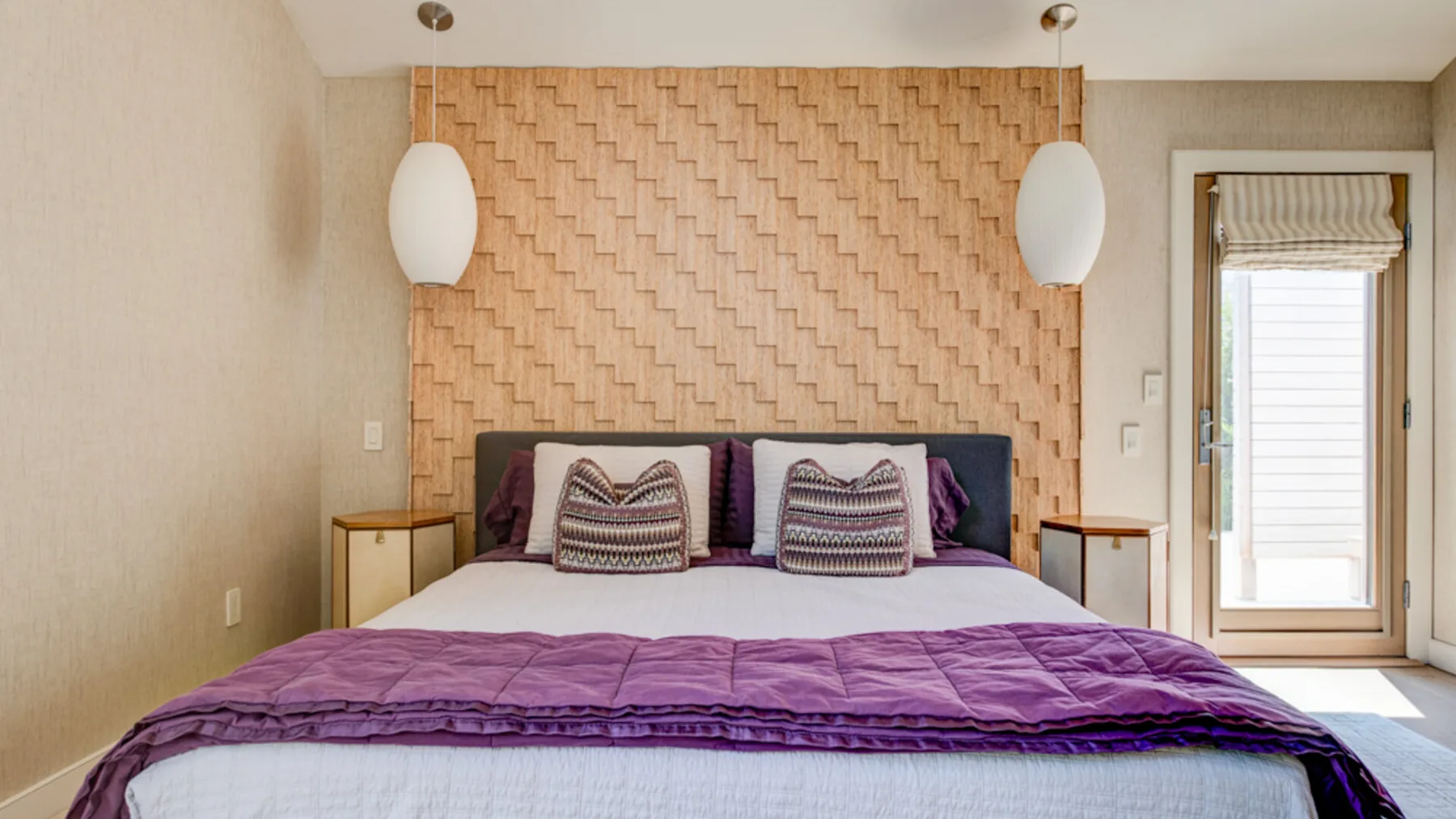 A bedroom with a large bed, patterned pillows, and two hanging lights.