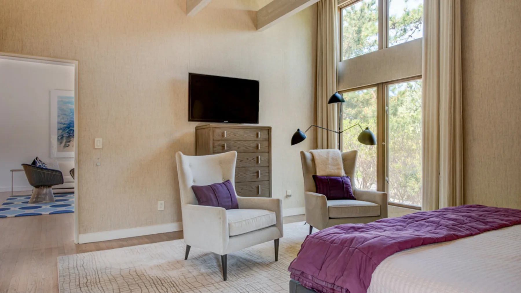 A bedroom with a bed, two armchairs, and a large window.