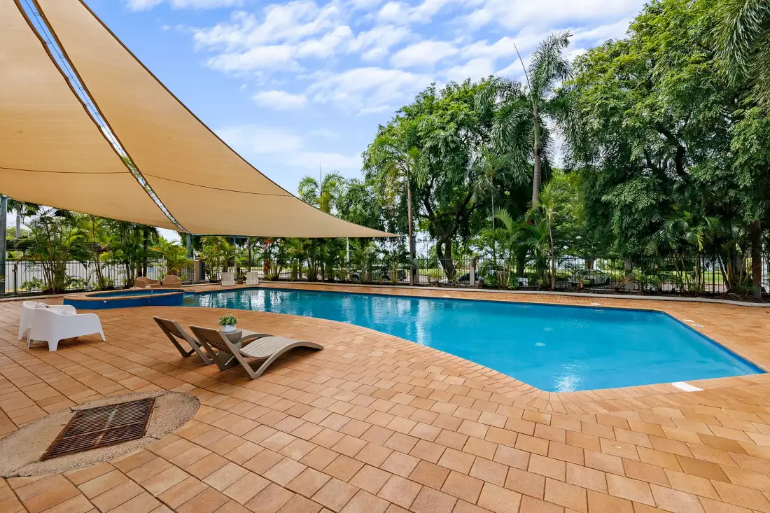 An outdoor swimming pool beside a tiled patio, shaded by a large canopy.