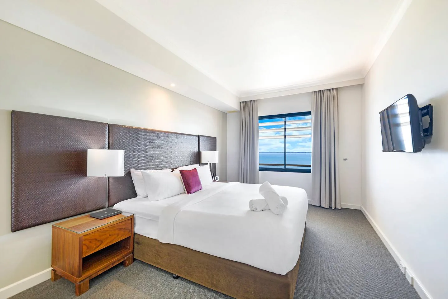 A bright bedroom with a bed, bedside tables, and a window overlooking the water.
