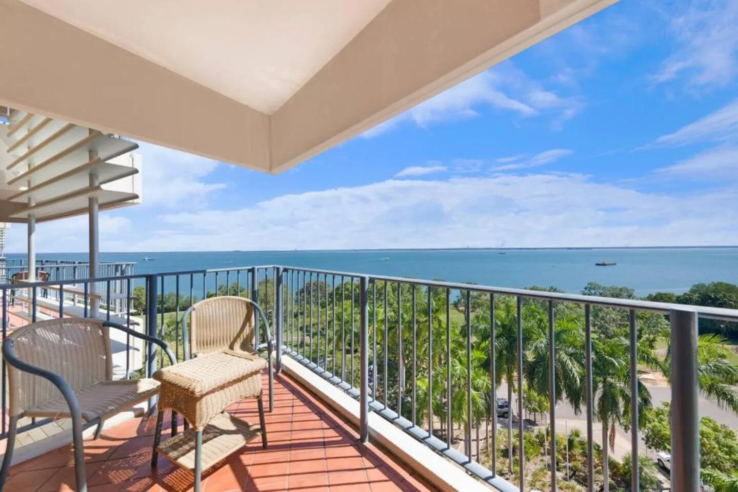 A covered balcony with seating overlooks the ocean and a tree-lined shore.