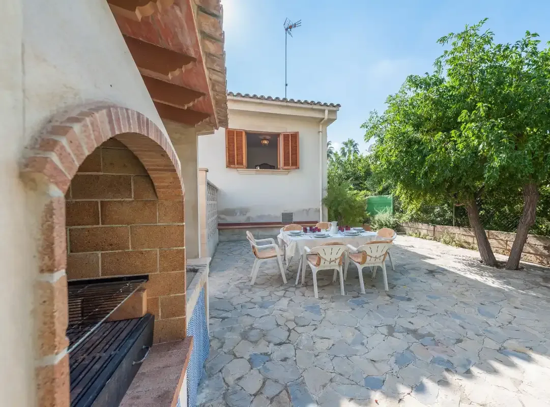 A stone-paved patio has an outdoor dining table beside a built-in barbecue.