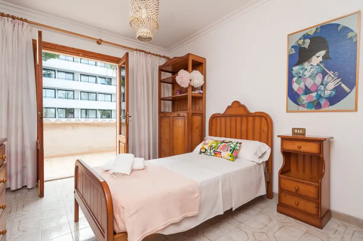 A bedroom with a wooden bed, bedside table, and open balcony door.