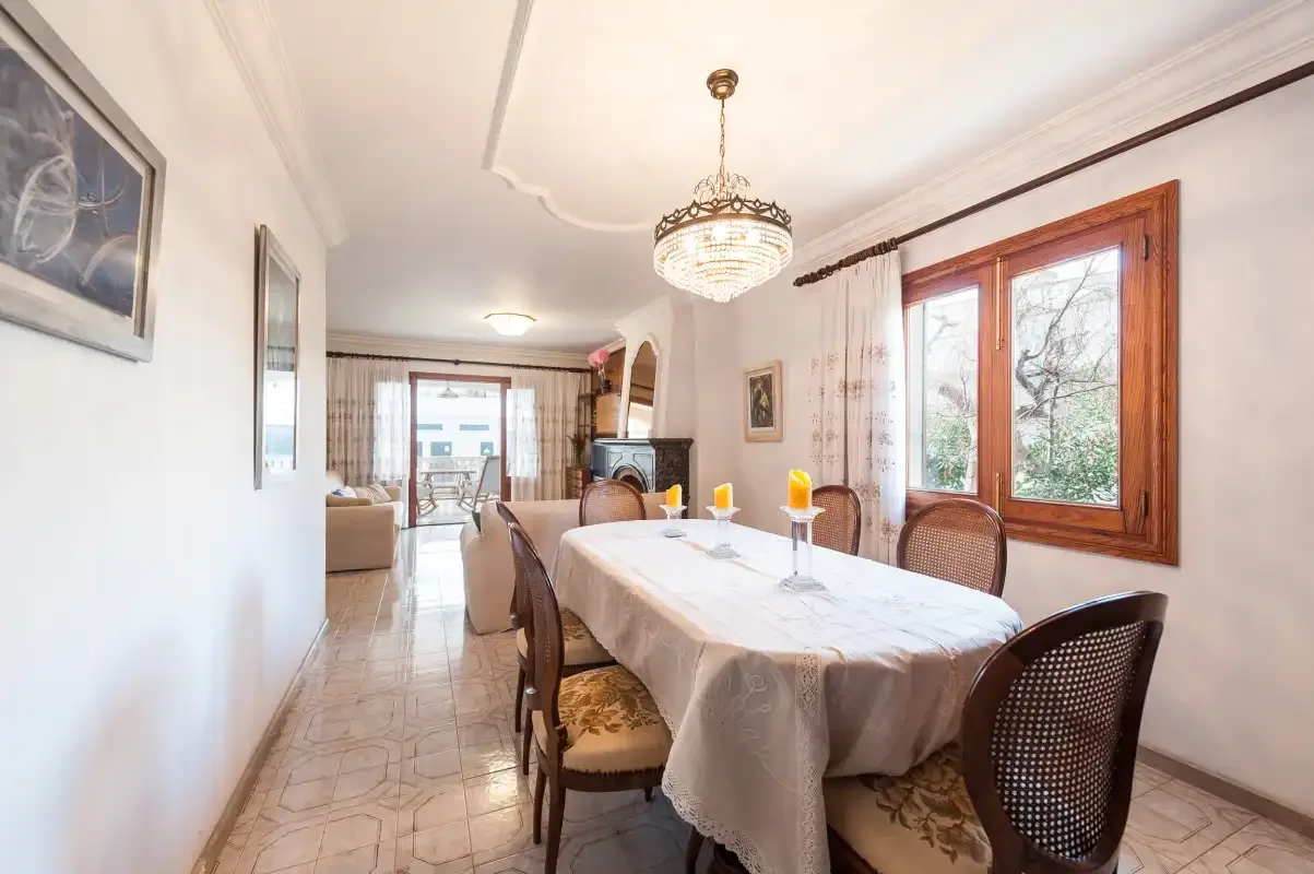 A dining room with a long table beneath a chandelier and beside a window.