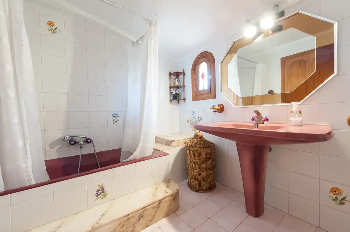 A tiled bathroom with a bathtub and a pink pedestal sink.