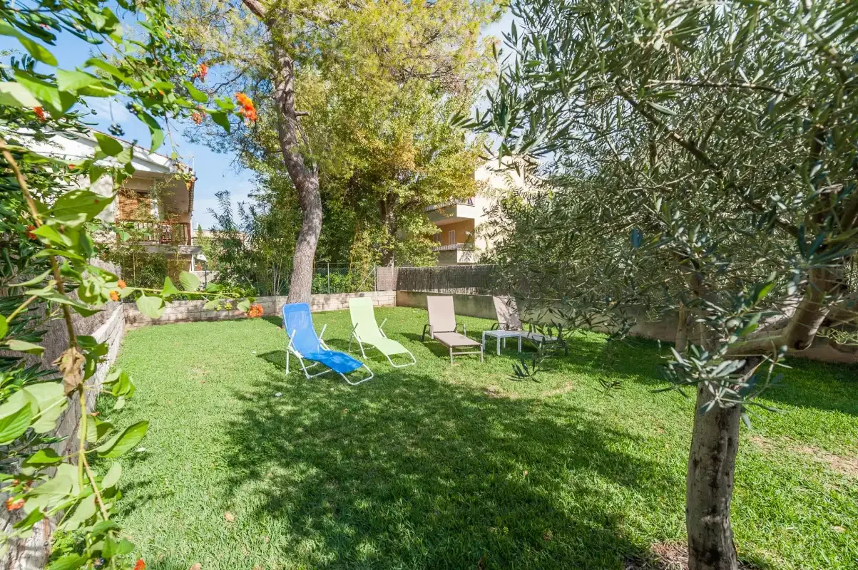 A grassy garden with outdoor seating beneath several leafy trees.