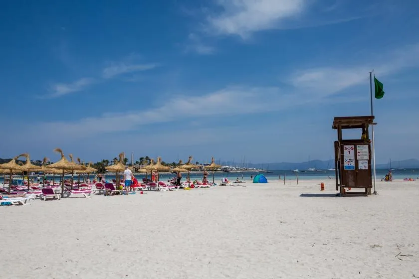 A sandy beach with rows of sunshades and a lifeguard tower beneath a blue sky.