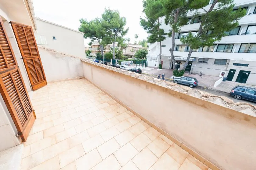 A tiled balcony overlooks a tree-lined street with parked cars.