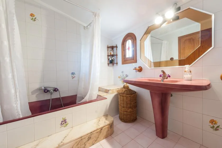A tiled bathroom with a bathtub, shower curtain, and sink beneath a large mirror.